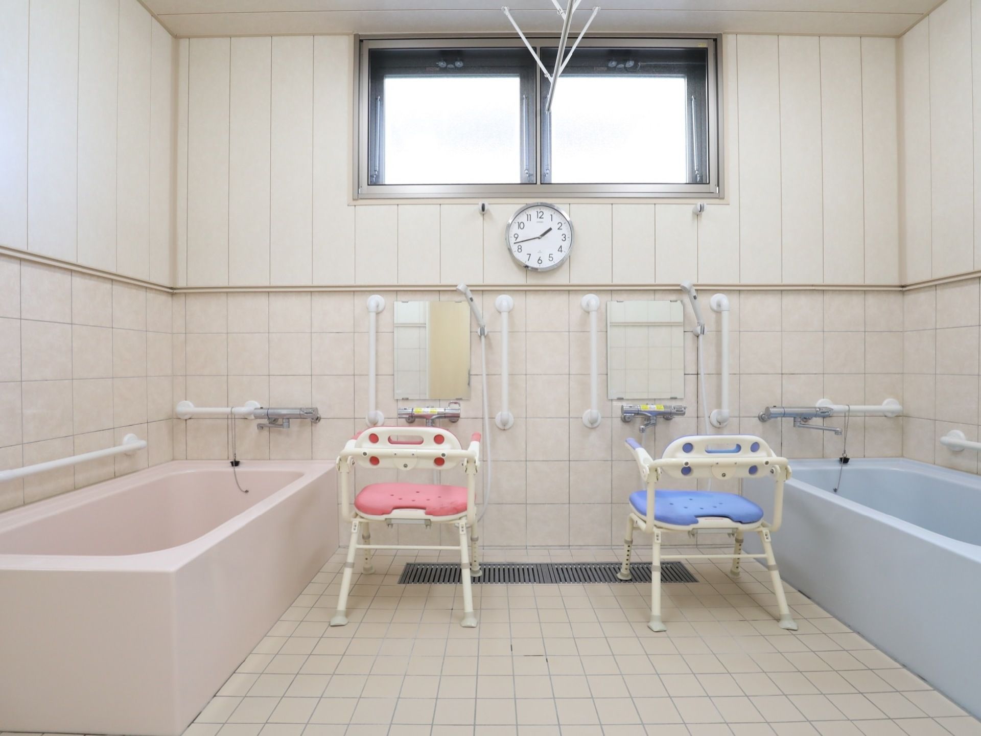 明るい浴室には、一人用の浴槽が二据え設置されている。シャワーチェアが２脚置かれ、その前には、蛇口、鏡、シャワーが備えつけられている。