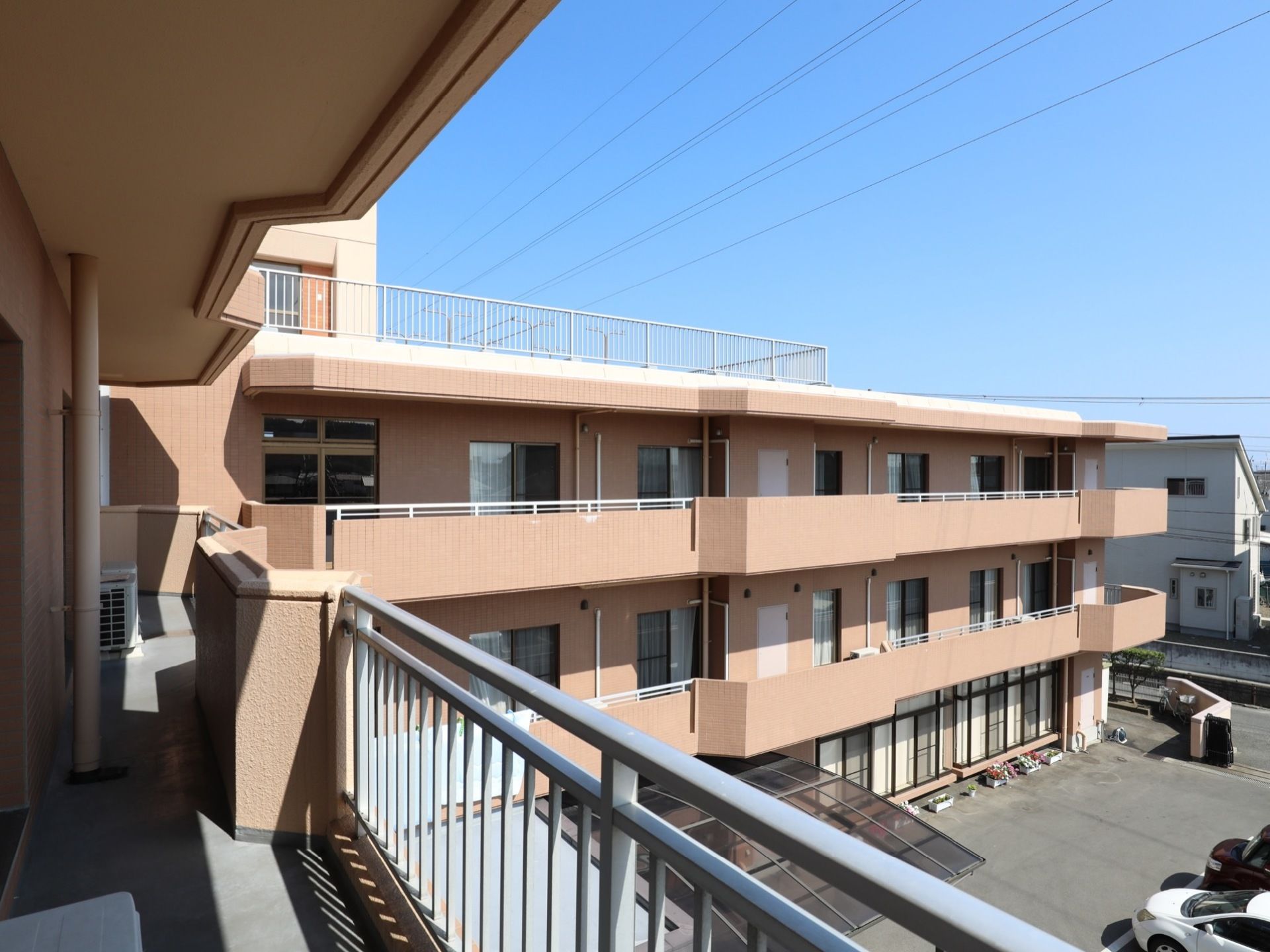 落ち着いたピンク色の３階建ての老人ホームである。Ｌ字に折れた建物の３階部分のベランダから広い中庭が見える。