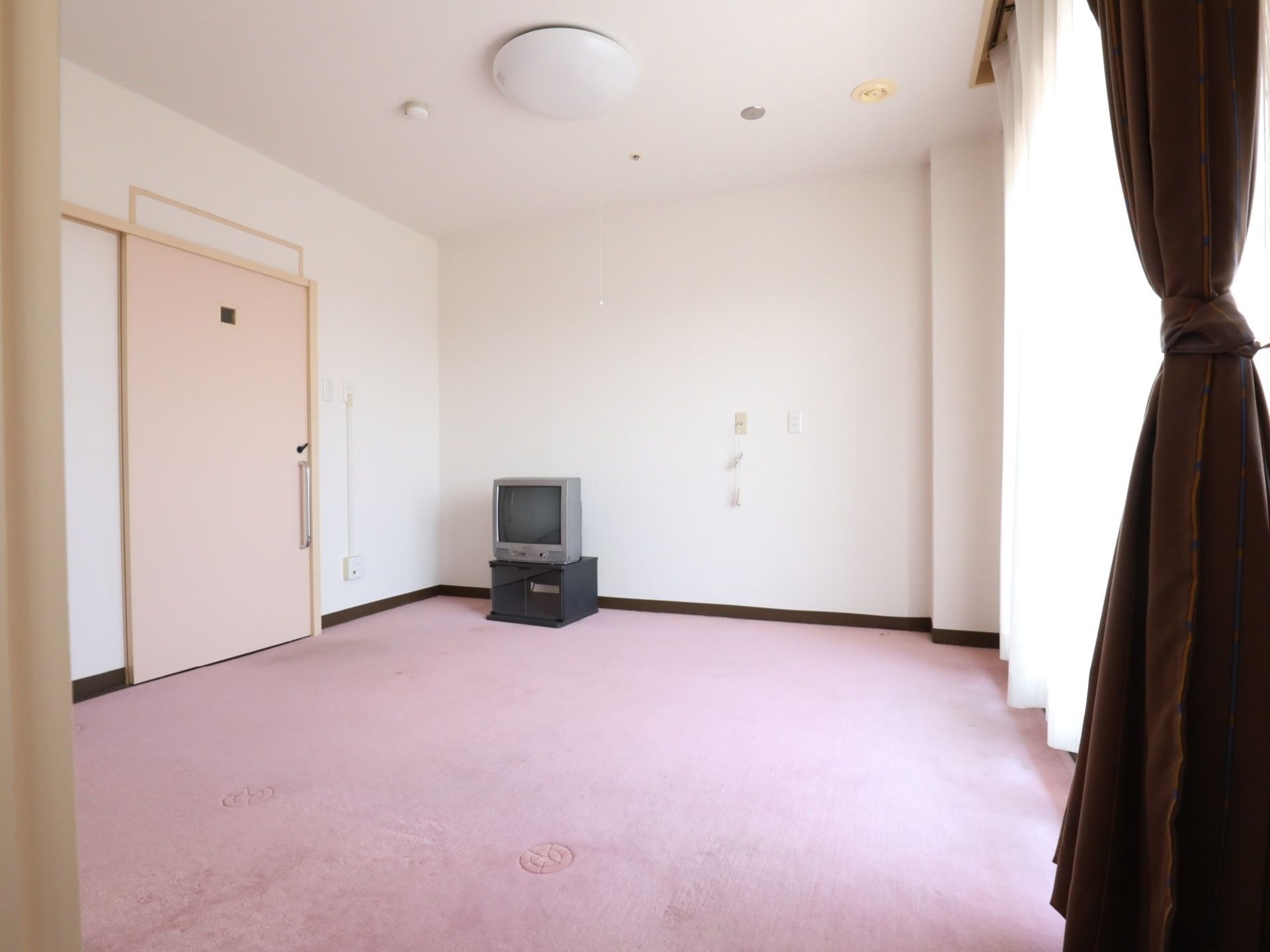 大きな窓があり広く明るい部屋にはスライドドアがついている。白い天井には照明や火災報知器が設置されていて、テレビもある。