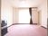 淡いピンクの絨毯が敷かれた部屋には大きな窓があり、明るい光が差し込んでいる。テレビが隅に置かれ、エアコンや火災報知器が設置されている。