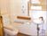 便座の両サイドに手や腕が乗せられる器具が設置してある。棚にはトイレットペーパーが複数ほど常備してある。