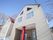白い壁に傾斜のついた屋根の２階建ての家屋が建っている。玄関部分が奥まっていて、雨雪に当たらないようになっている。