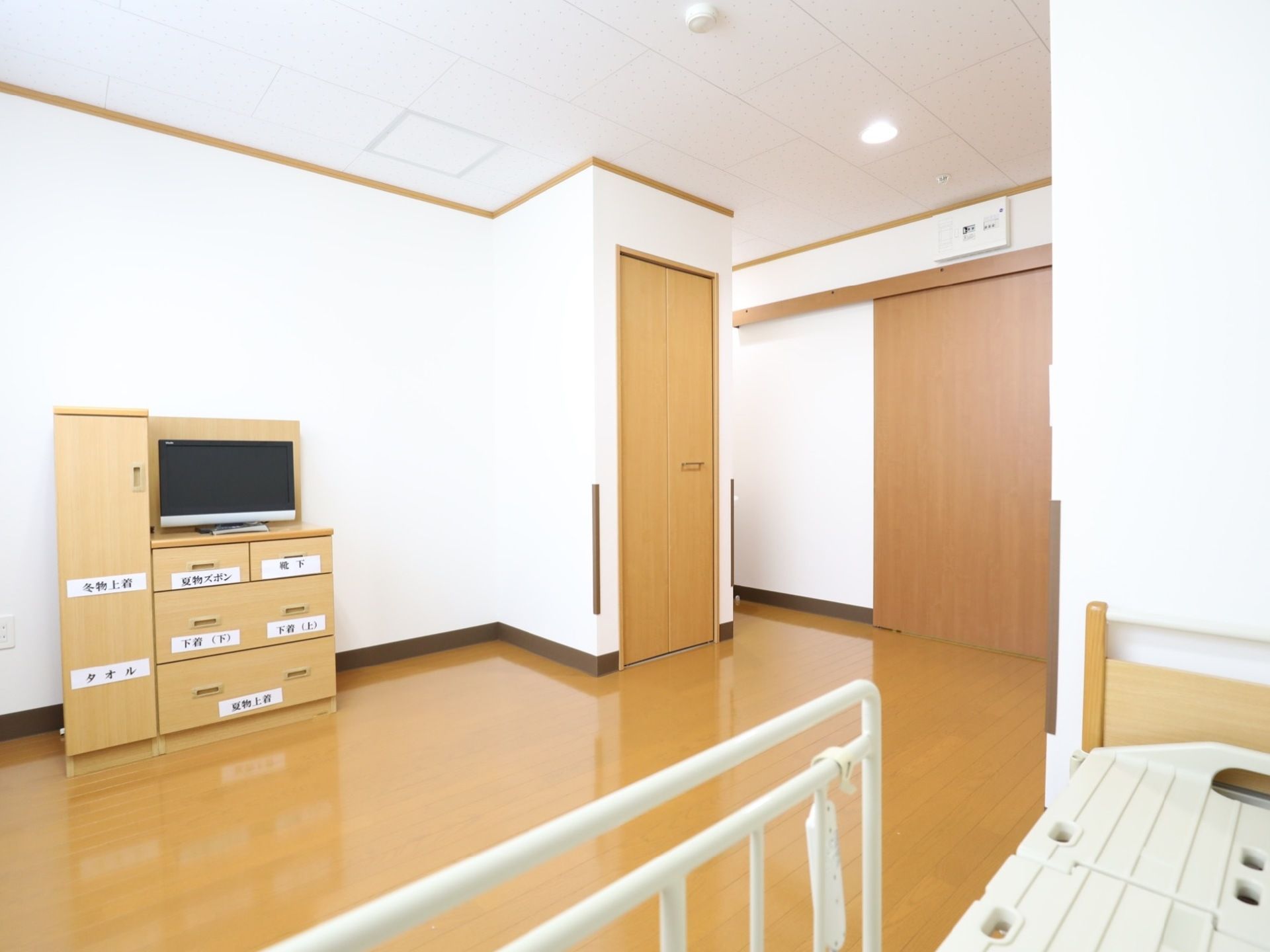 フローリング敷の広々とした居室。入り口の扉は広く開閉する引き戸になっている。テレビ台を兼ねた収納スペースには衣類が収納されている。