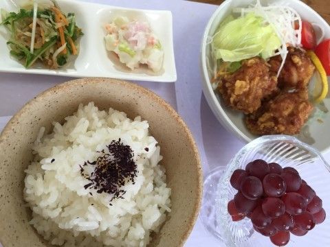 食事の一例。一汁三菜の食事に、デザートが付いている。メイン料理はから揚げで、サラダとブドウが出されている。