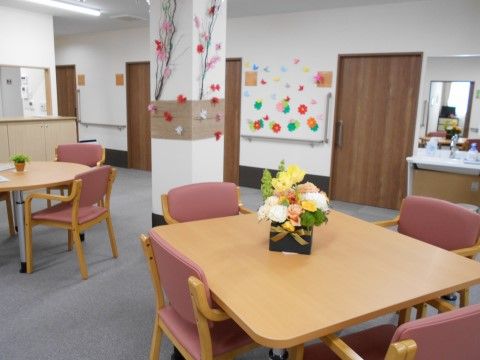 壁に手作りで制作された作品が飾られており、心が和む空間である。入居者様同士が座れるテーブルには花が置かれている。