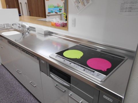 清潔感あるステンレス製のシステムキッチンがある。IH調理器が設置され、マットを敷くなどお手入れしやすい工夫をしている。