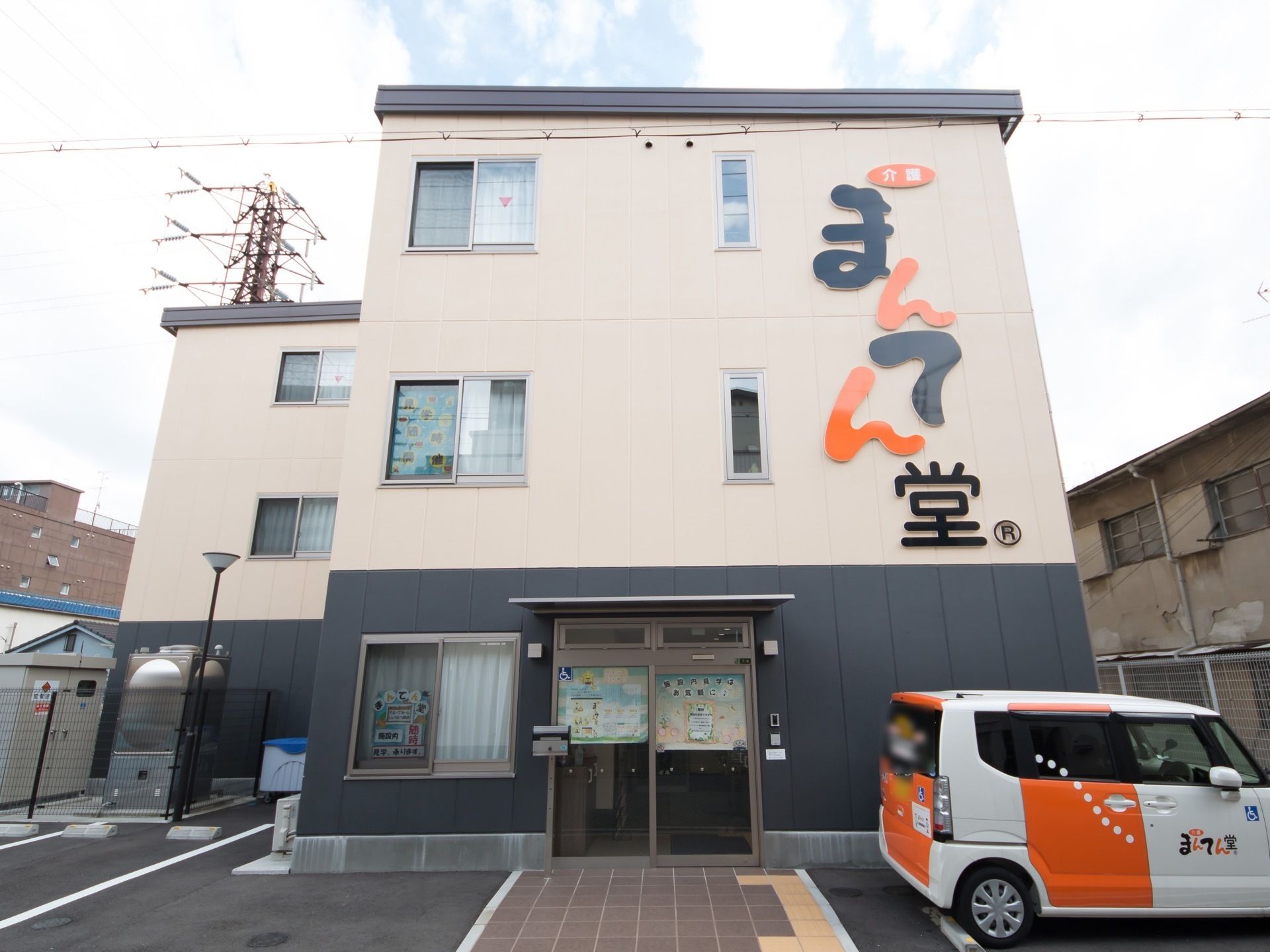シンプルな作りの、綺麗で新しく見える外観。送迎用の社用車が停まっており、来訪者様用にも駐車スペースが二台分ある。