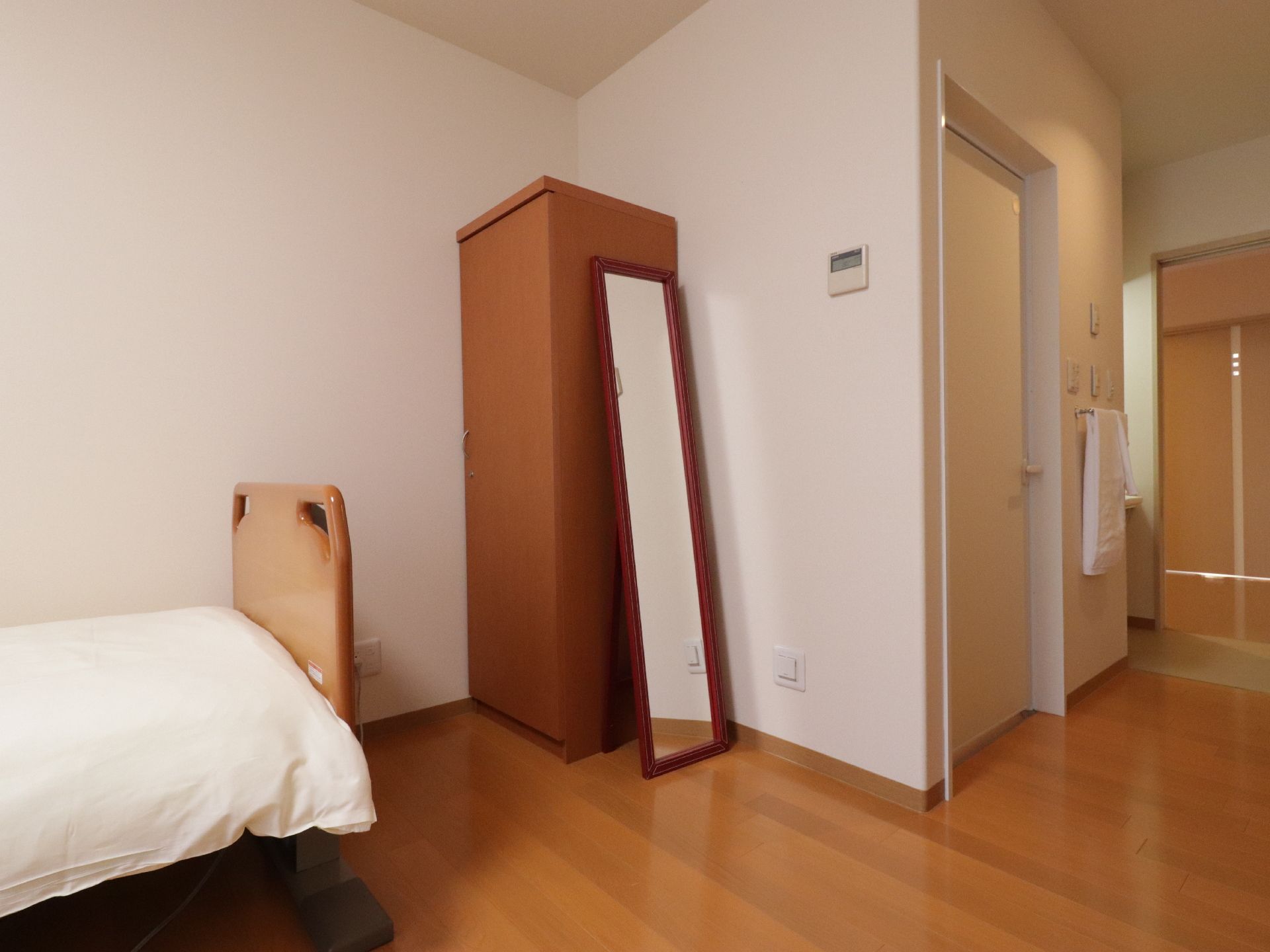 出入口から入って右側に洗面台を備えている。部屋の角には、木目調の片開きのクローゼットを置き、隣には、ベッドを置いている。
