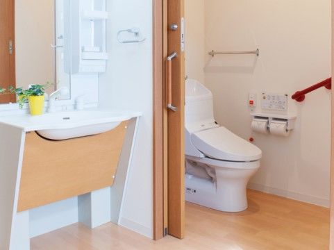 トイレの中には手すりが備え付けられている。引き戸になっており、段差もないため出入りがしやすく、洗面台もシンプルで使いやすい。