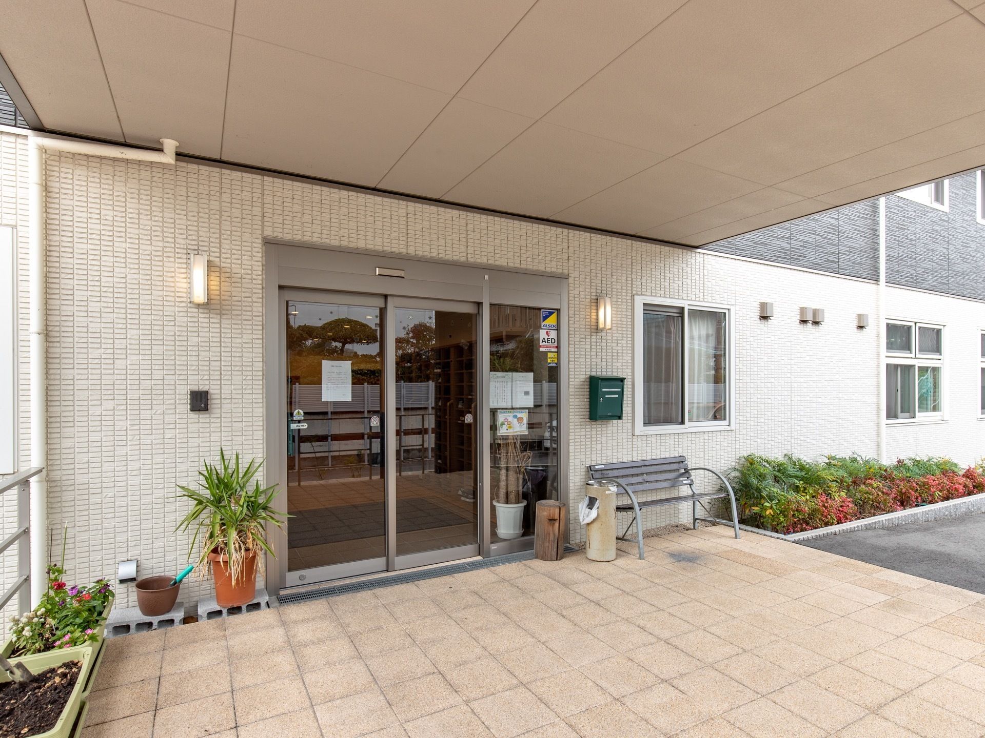 玄関前は広々としたスペースがあり、屋根も設置されている。入口には、ガラス張りの自動ドアが取りつけられている。