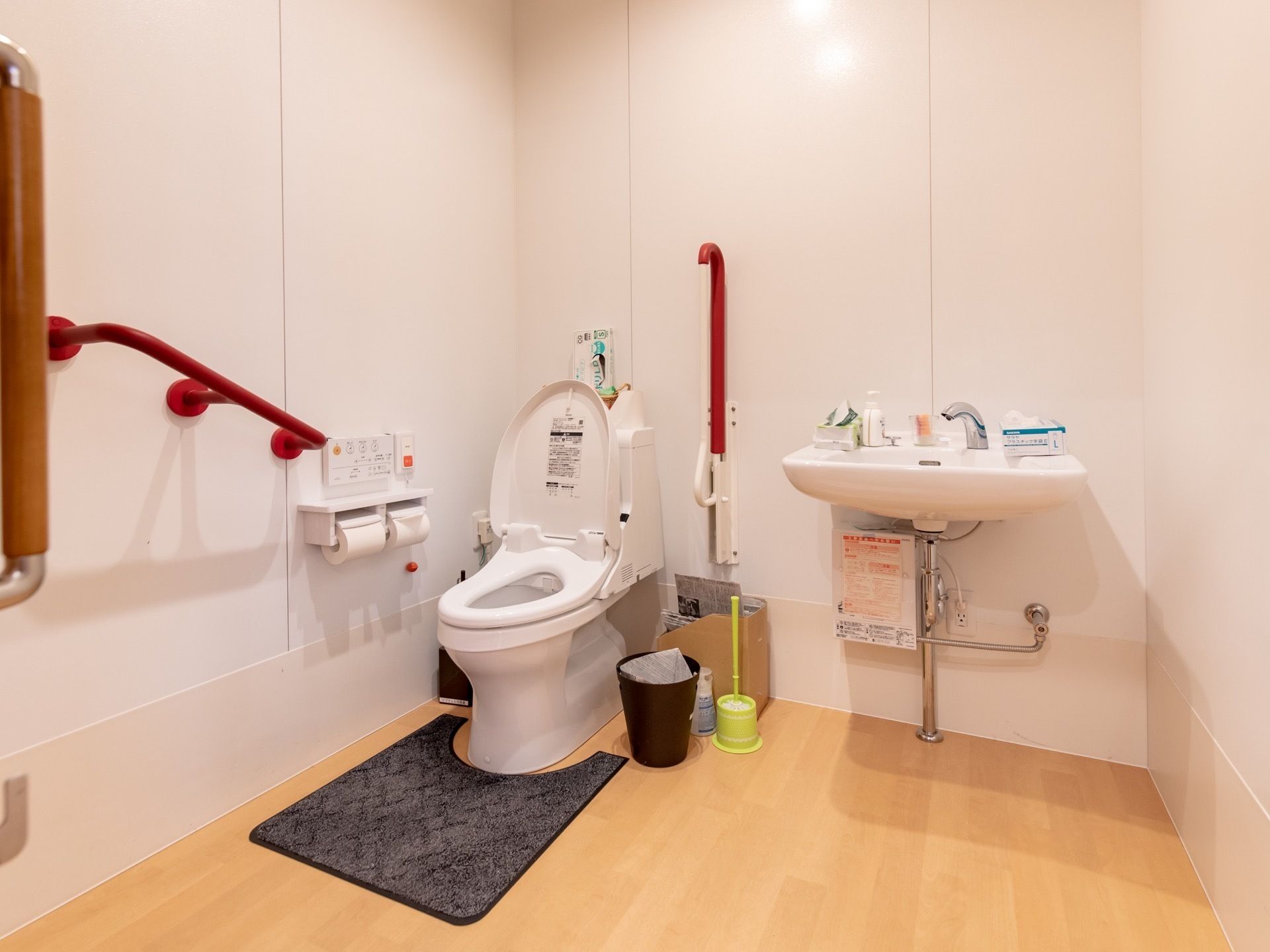 室内は全面フローリングで、トイレと手洗い場が隣同士で設置されている。壁には、赤色と茶色の手すりが取りつけられている。
