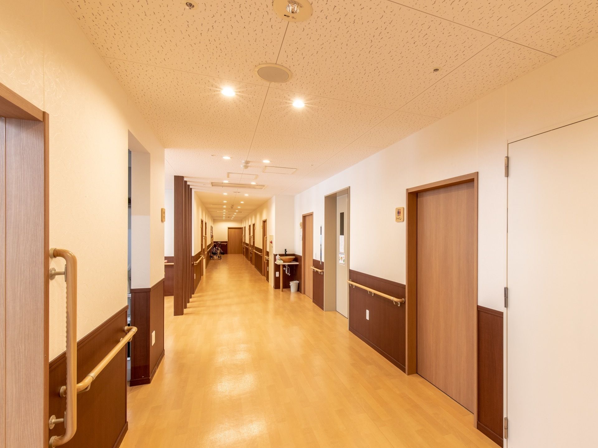 廊下は広々としており、両サイドには入居者様用の居室がたくさん並んでいる。入口には、大きな引戸が取りつけられている。