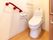 トイレは、広々としたスペースが確保されている。壁には、赤色の手すりやタオル掛け、トイレットペーパー掛けが設置されている。