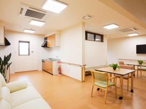 白いソファと観葉植物が置かれた広々としたフロアにシステムキッチンが設置されている。壁に薄型テレビが掛けられている。