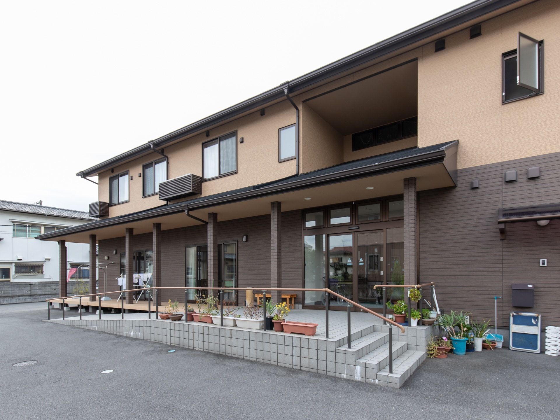 ブラウンを基調とした外観の２階建ての建物である。玄関前には階段とスロープが取りつけられている。周囲には植物が置かれている。