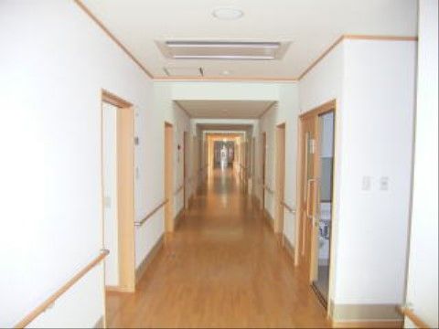 真っすぐに伸びた居室前の廊下は、温かみのあるフローリング敷になっている。白い壁には手すりが設置されている。