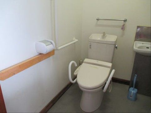 白い壁紙の室内に、手すり付きの洋式便座がある。また、その周囲の壁面にも手すりが設置され、安全面に非常に配慮されている。