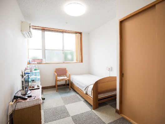 寝具付きのベッドが置かれた部屋にはいすやタンス、テレビなどもあり、大きな窓が付いている。