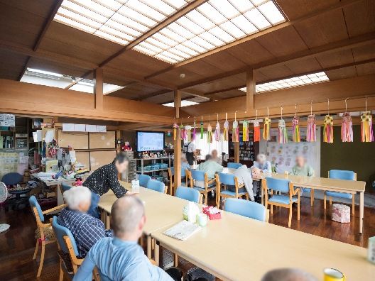 大きなダイニングテーブルセットが複数置かれた食堂。椅子に座ってくつろいでいる入居者が複数名いる。