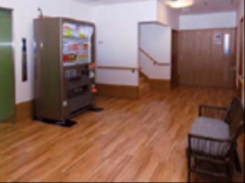 エレベーターの前の共有スペースに、自動販売機が設置されている。床はフローリングで、ソファも置かれている。