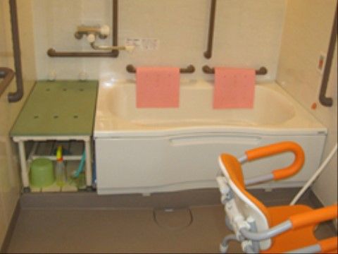 浴室内の壁にたくさんの手すりが設置されている。洗い場にはシャワーチェアが置かれ、壁にナースコールが備わっている。