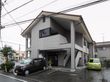 灰色を基調とした外壁の２階建ての施設である。玄関前にゆるやかなスロープがあり、その横に車が停められている。