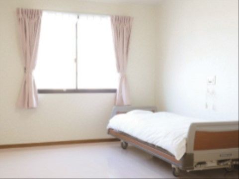 腰高窓があるシンプルな室内は、壁も床も白く清潔で明るい印象。低床型のベッド横には緊急呼び出しボタンが設置されている。