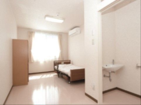 居室にはリクライニング機能がついた、介護用ベッドが置かれている。また室内にはタンスがあり、エアコンが用意されている。