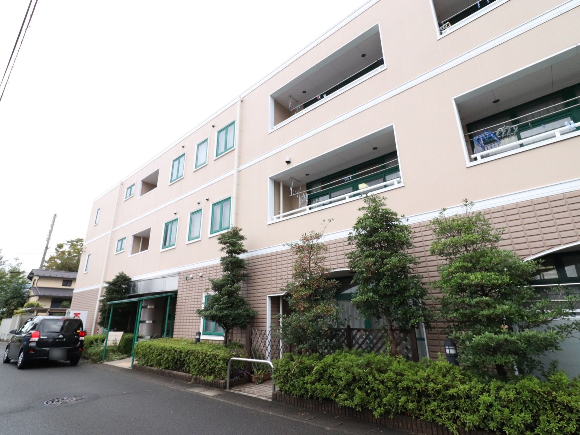 ３階建ての建物で、外壁は薄いピンク色である。施設の前には植え込みがあり、木がたくさん植えられている。