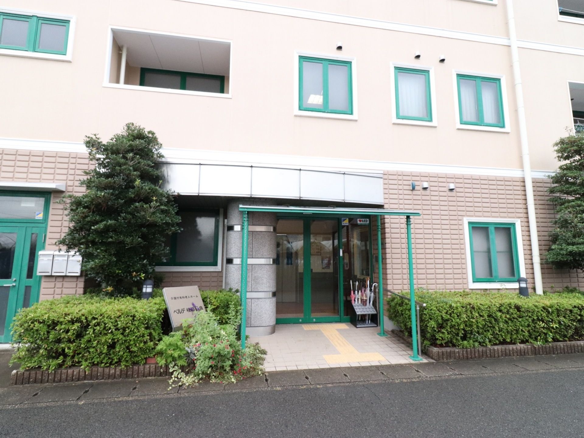 玄関の左側には施設名の看板が設置されている。道路から玄関までは屋根を設置しており、床のタイルには点字ブロックがある。