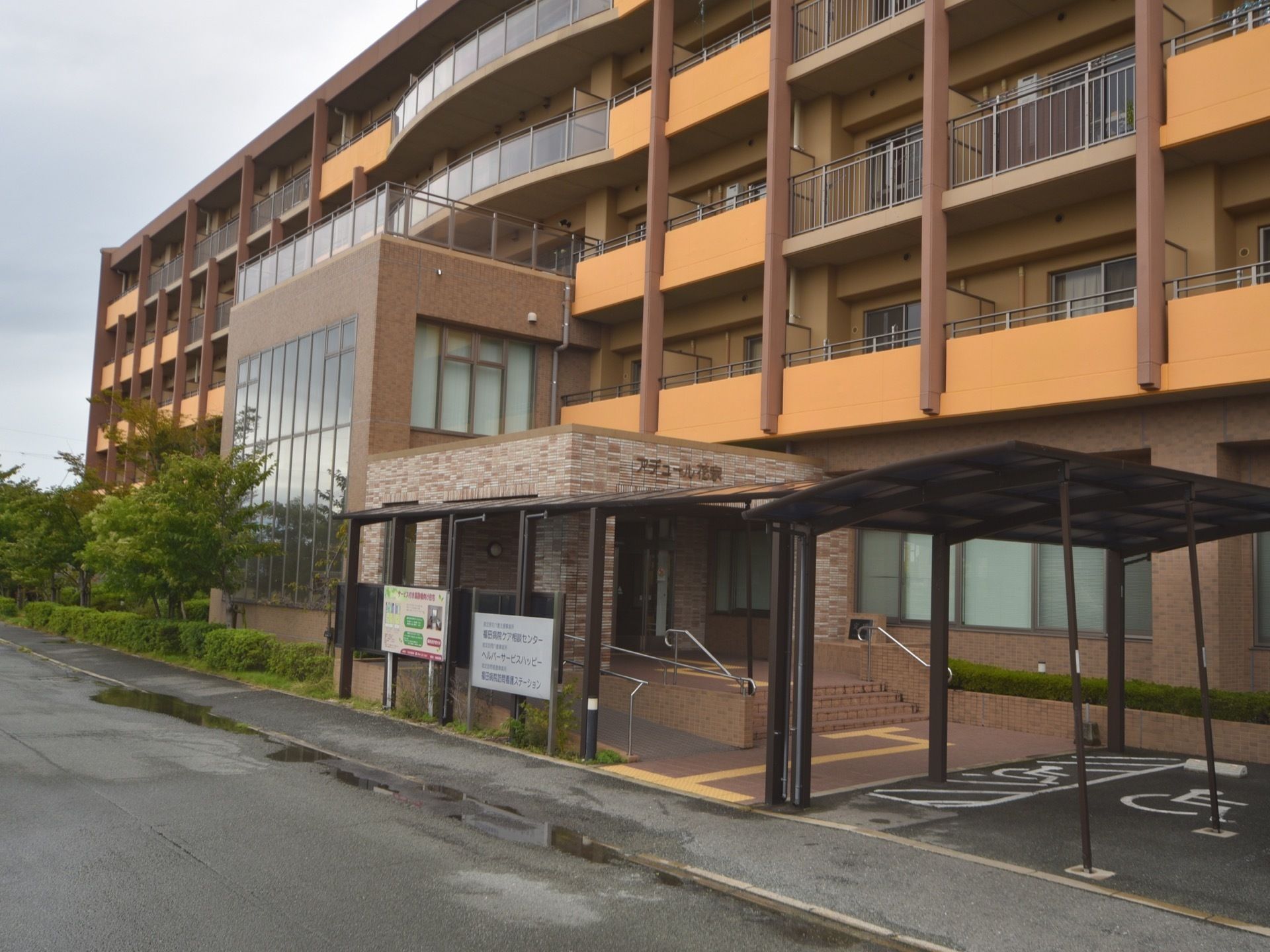 茶色とオレンジ色が基調の建物で５階建てになっている。玄関までは手すり付きの階段とスロープ両方が設置されている。