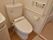 洗面台と浴室の間に洋式トイレが設置されている。温水洗浄便座のボタンや手すり、呼び出しボタンが左側にある壁に取り付けられている。