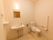 白をメインとした、手洗い場つきのトイレである。温水洗浄便座を完備している。可動式の手すりも備えつけられている。