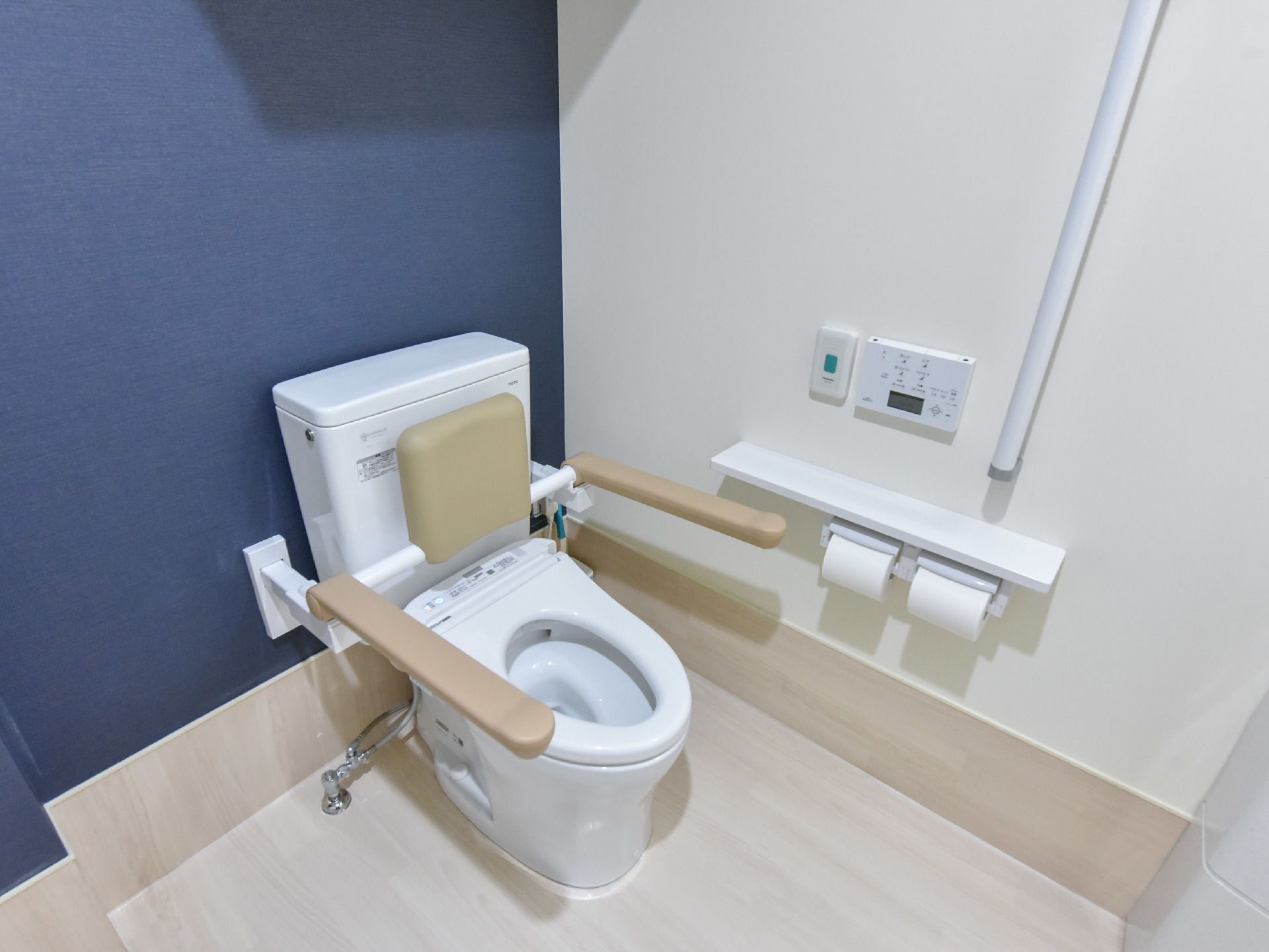 壁や便座には手すりが設置されている。壁にはウォシュレットのボタンやナースコールがあり、背もたれが便座についている。