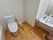 白い壁とブラウンのフローリング敷の広々としたトイレには、大きな鏡が取り付けられている洗面台が設置されている。