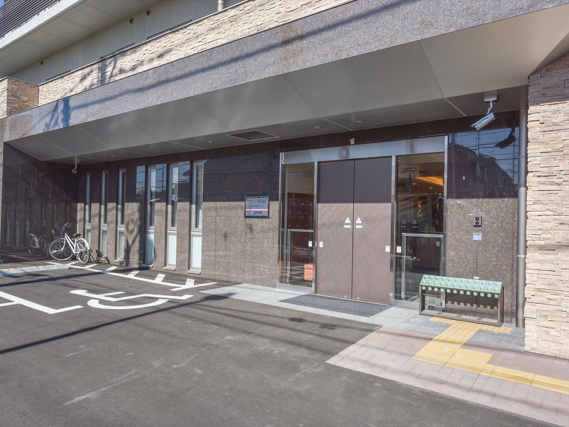 玄関の前は広くなっている。扉は自動ドア。傘立てが置かれている。足元はバリアフリーで、点字ブロックもある。