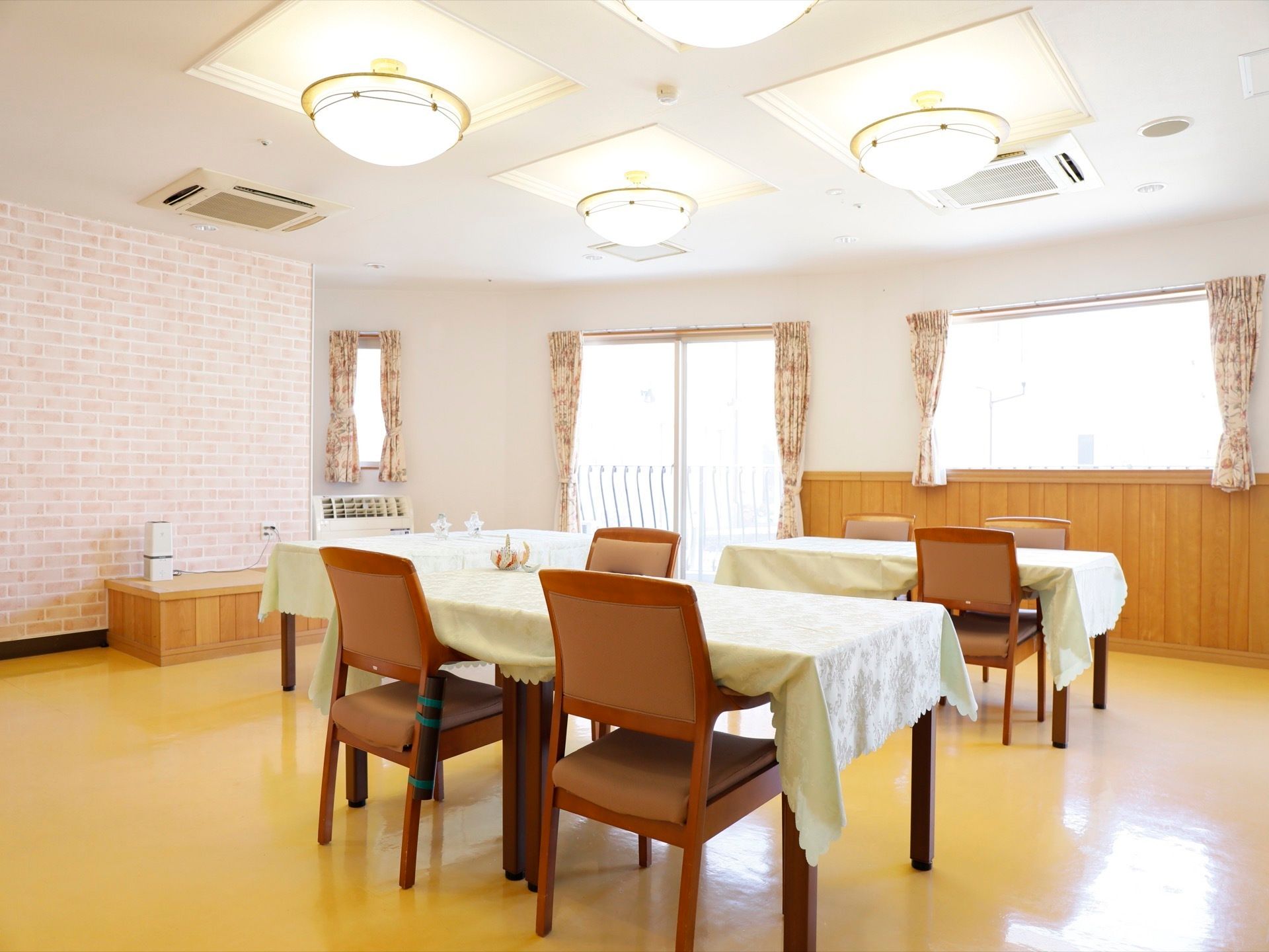 壁の一部が、煉瓦調の壁紙になっている。天井には複数の照明とエアコンが設置されている。クロスの掛かったテーブルもある。