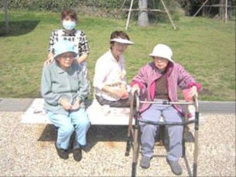屋外のベンチに座って日光浴しているご入居様とスタッフ