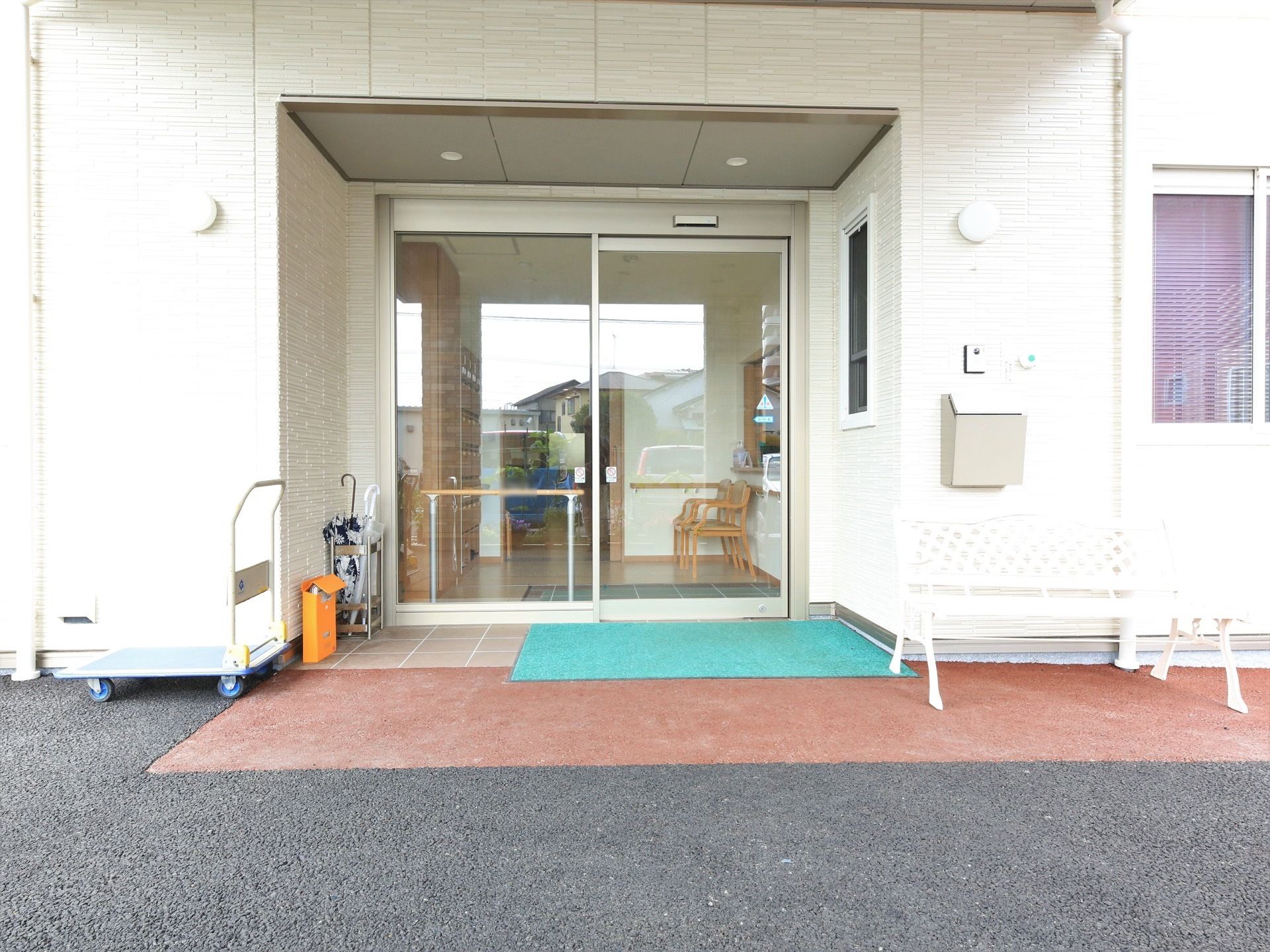 玄関扉はガラス張りの自動ドアになっていて、室内の様子が透けて見える。出入口の床にはマットが敷かれ、端に傘立てが置いてある。