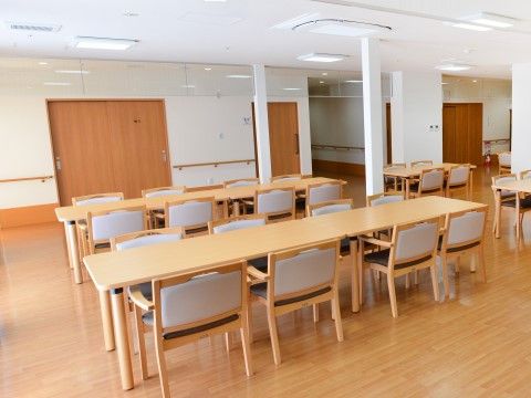 明るい木目調のテーブルが並んでいる。椅子には肘掛けが付いている。室内は清潔感があり、照明も十分で明るい。