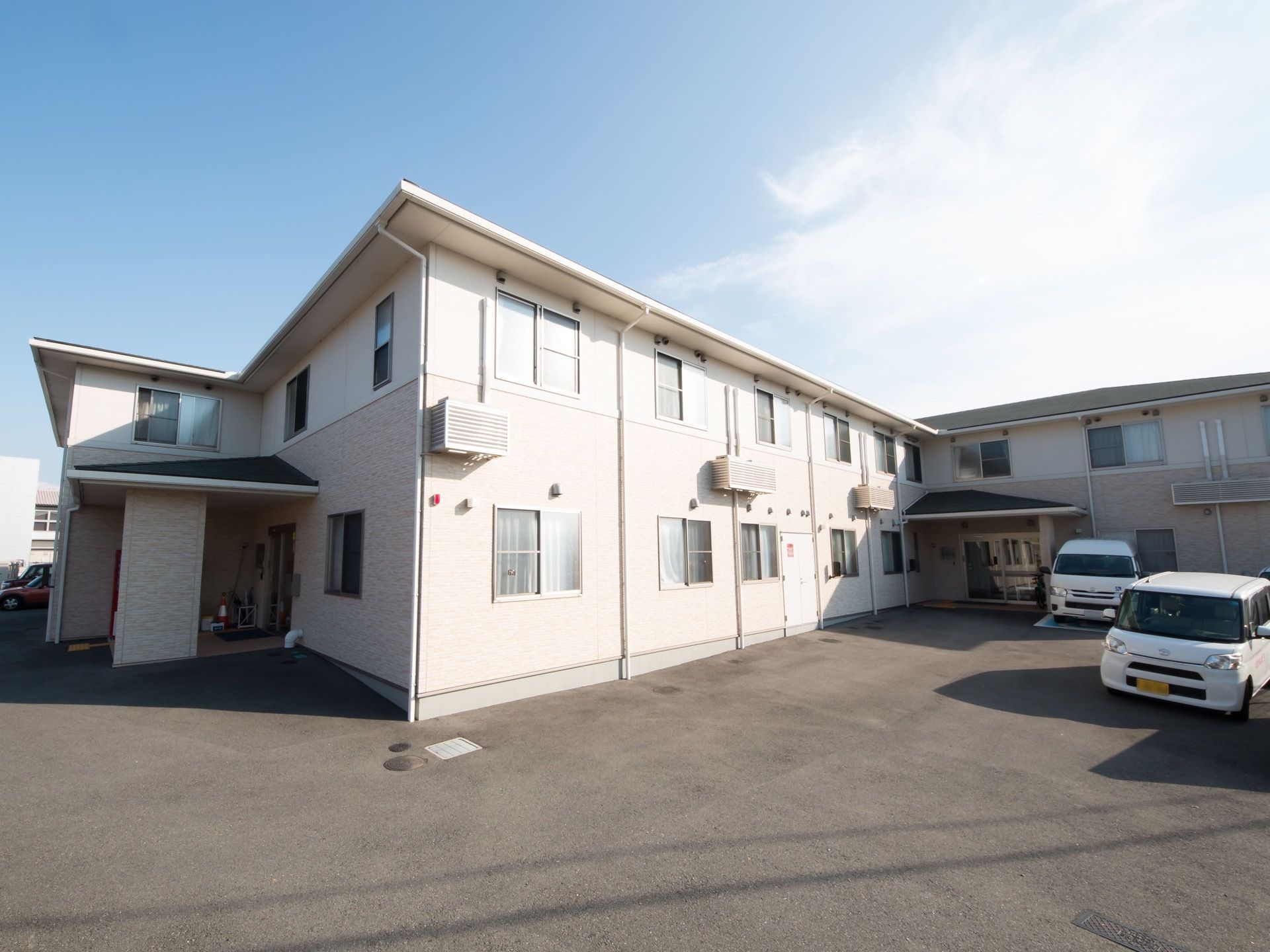 施設は２階建てで、日当たりに大変恵まれている。建物の周囲に何台か車が駐車されている。敷地内に段差は見られない。
