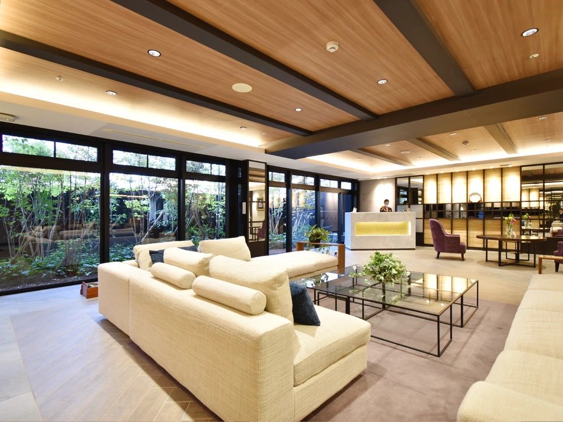 高級ホテルのロビーのような空間。ガラスのテーブルを囲むように大きなソファが置かれている。後方には大きな花が置かれている。