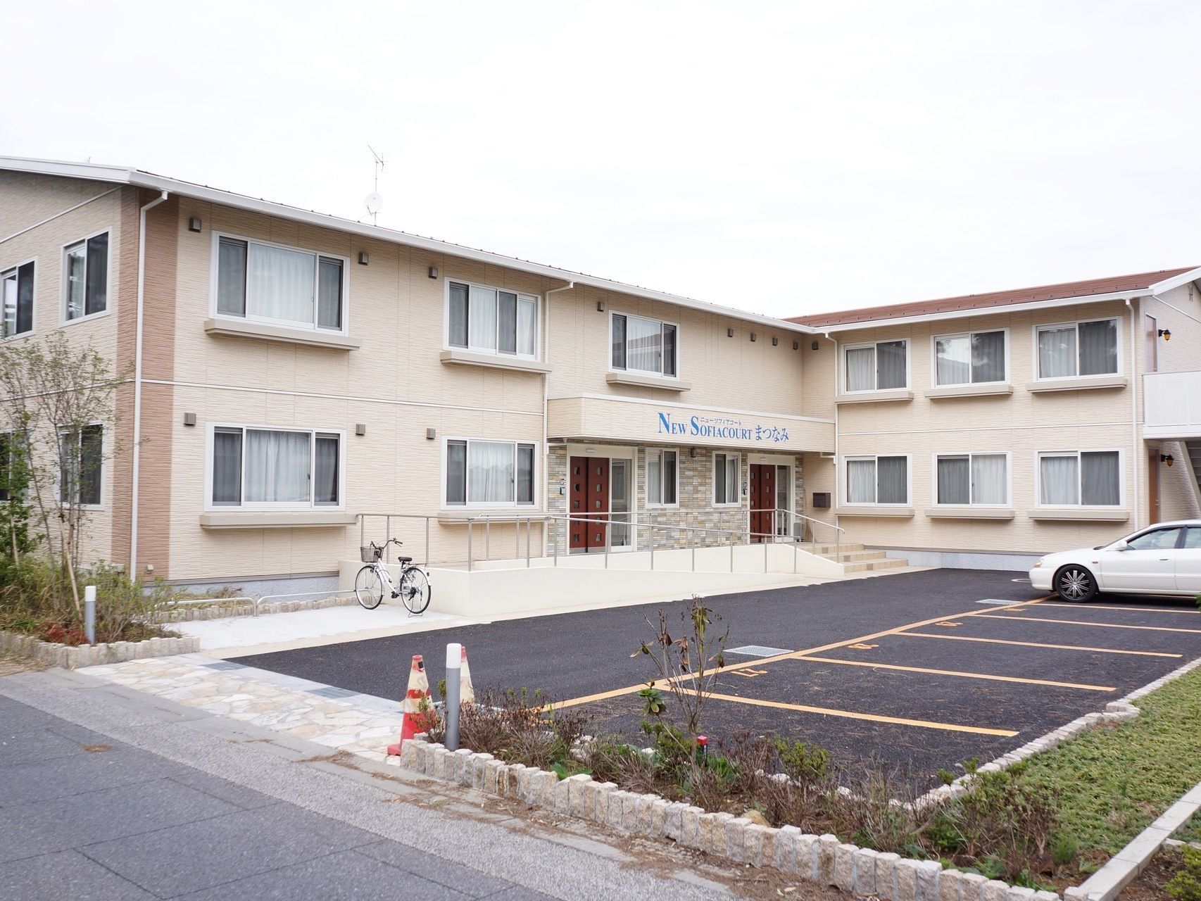 施設はベージュ色の壁で２階建てである。敷地内に駐車場と駐輪場が完備されている。施設を囲むように木や植物が植えられている。