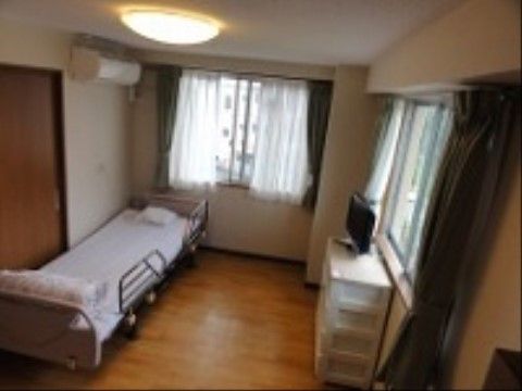 エアコンが完備された個室タイプの居室である。フローリングの床の上にはベッドや洋服ダンス、テレビが設置されている。