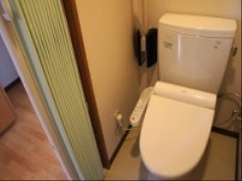 居室に備え付けられた温水洗浄機能付きの洋式トイレである。取っ手の付いたカーテンで仕切られるようになっている。