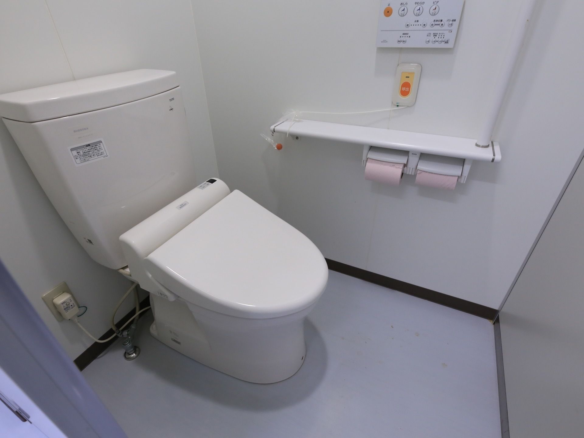 共用の個室トイレ。壁には手すりとトイレットペーパーに加え、ナースコールと温水洗浄便器のコントロールパネルがある。