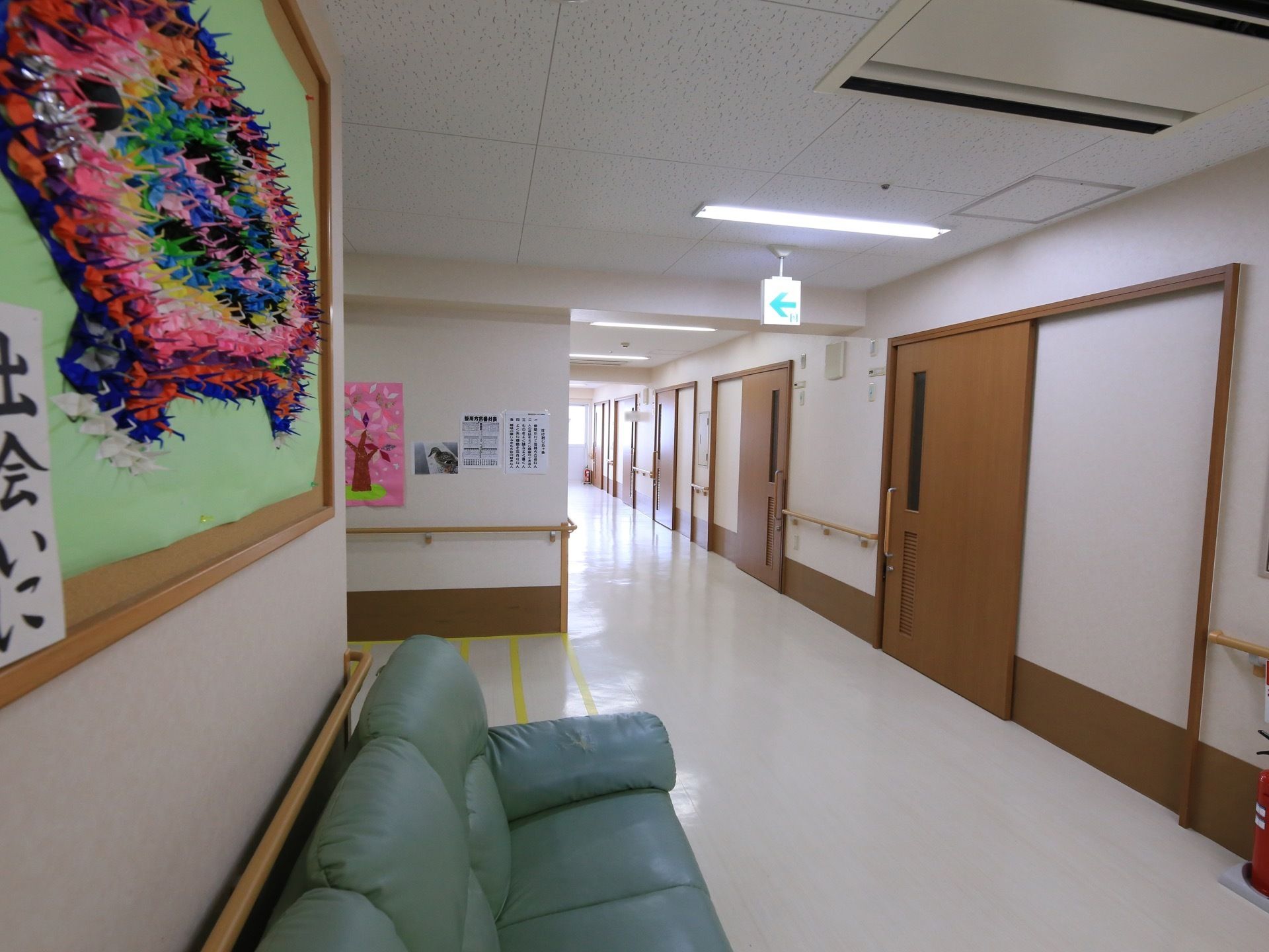 施設内の廊下の様子。談話スペースになっている所は少しだけ広くなっている。天井には非常口の誘導灯が取りつけてある。