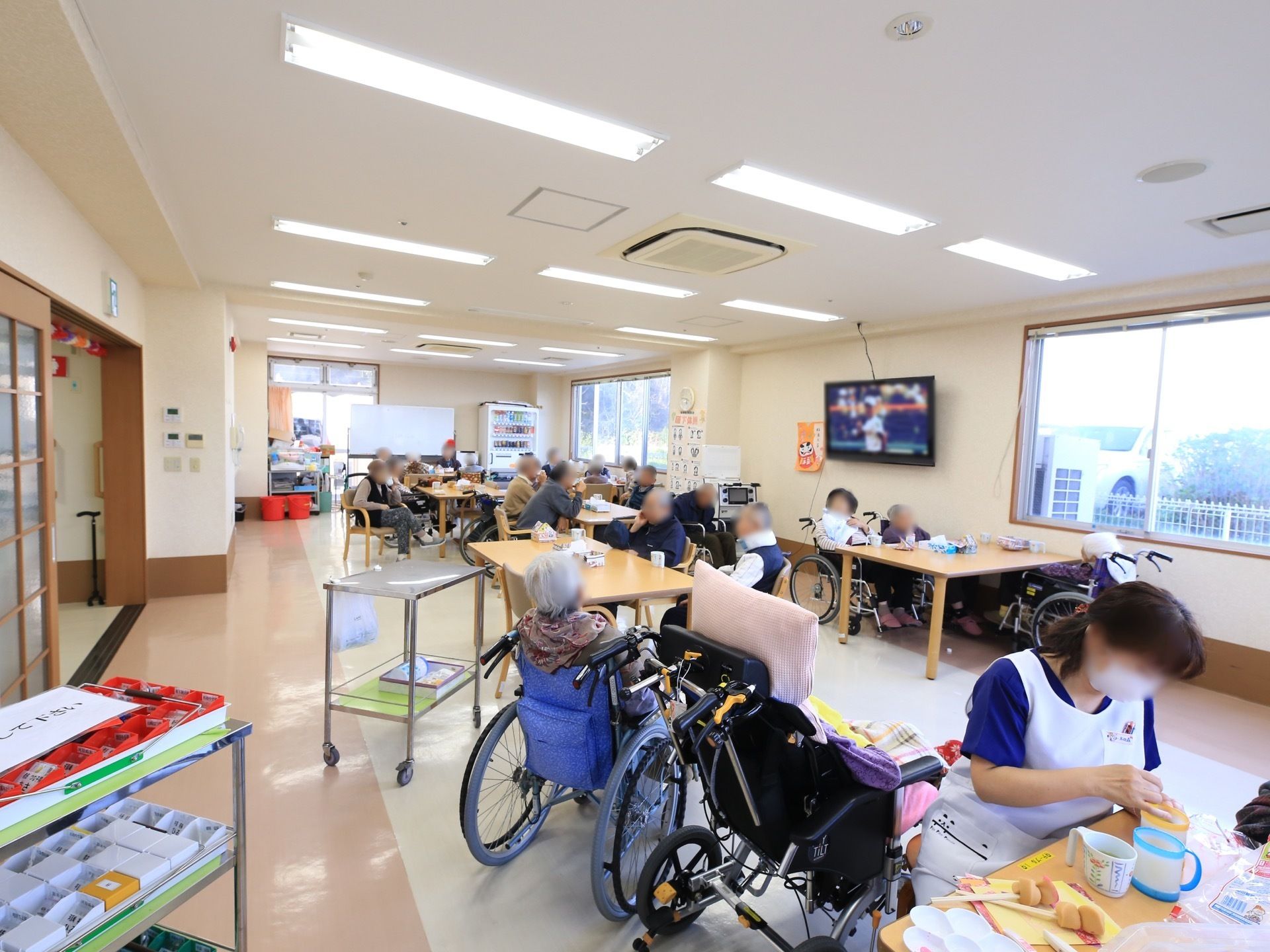 大きな食堂兼共有リビングには、日々多くの入居者様が集まっている。窓側の壁には大きな壁掛け式のテレビが設置されている。
