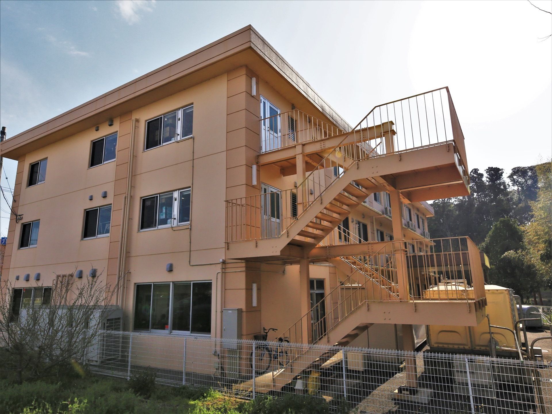 建物本体はオレンジ色がかったカラーをした３階建て構造になっている。正面の道路に対して裏手には屋外階段が取りつけてある。