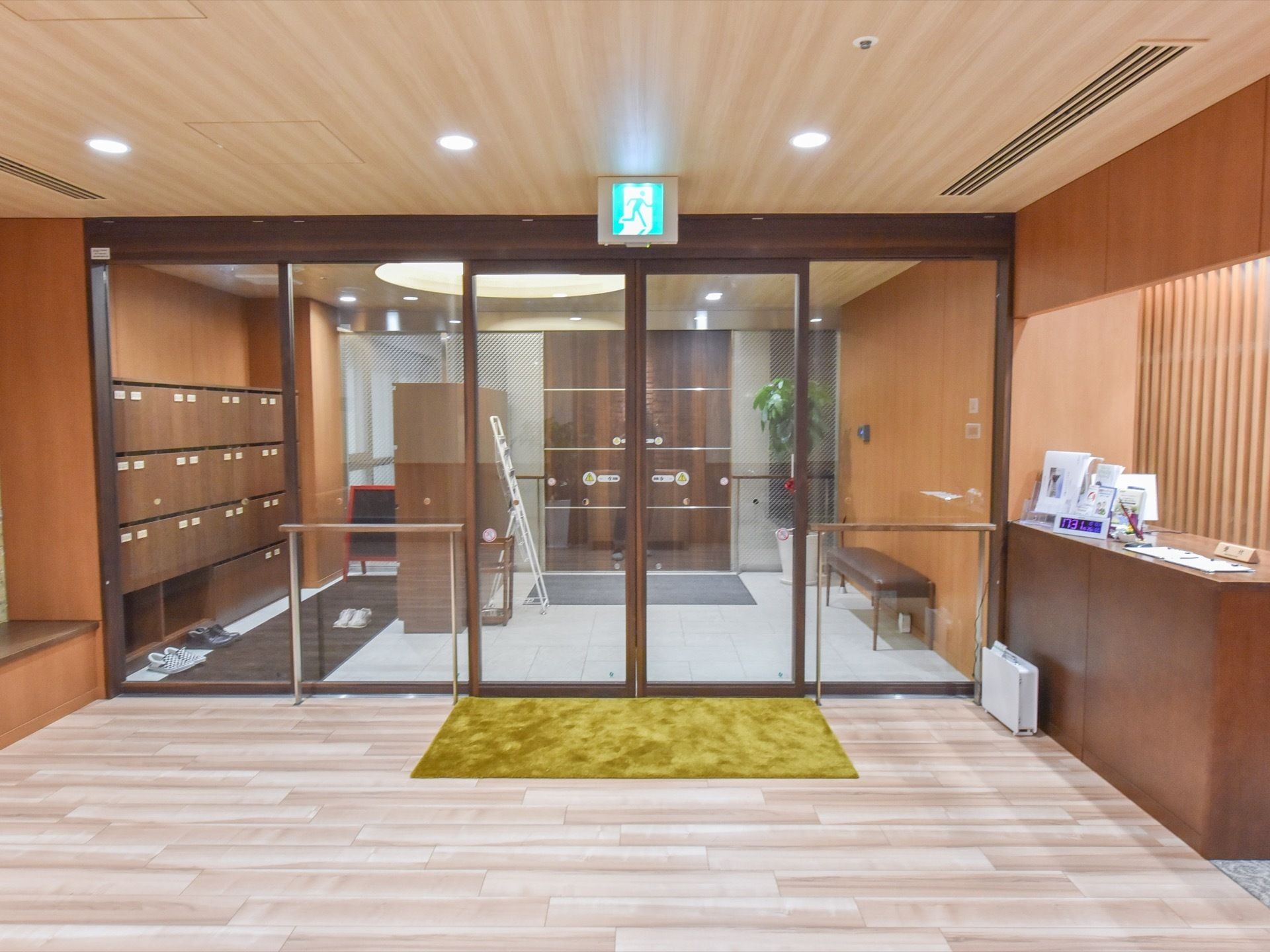 ガラス張りの自動ドアの向こうに、大きな靴箱が設置されているのが見える。右端には、長椅子や観葉植物が置いてある。